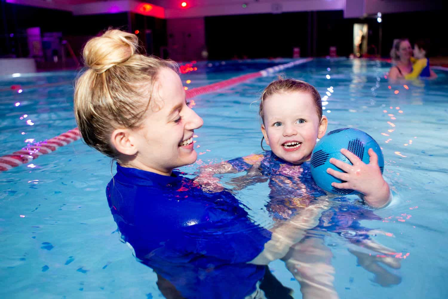 Swimming instructor and children sat on edge of swimming pool