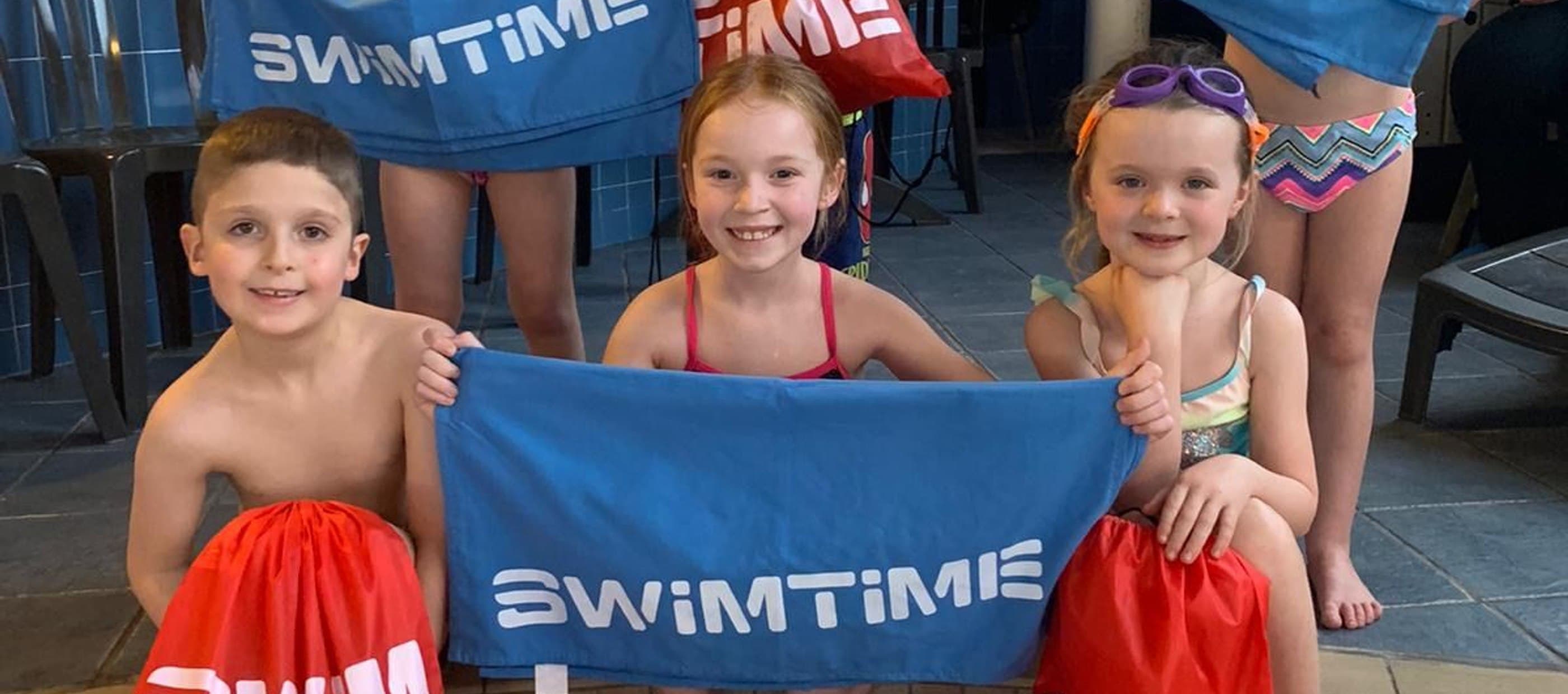 Children holding bags and towels with Swimtime logo